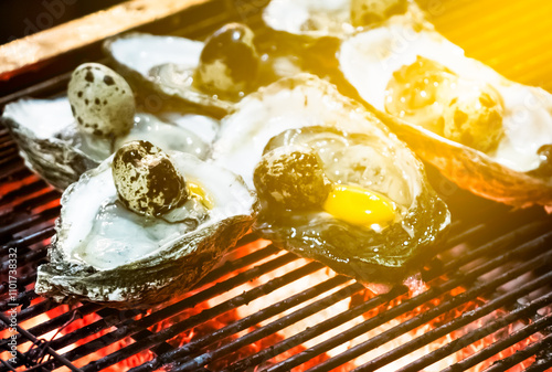 Chargrilled oysters with quail eggs cooking on a grill with flames and smoke. Asian street food concept