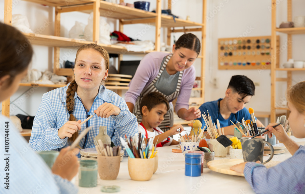 Joyful children, together with the teacher, paint ceramics with brushes at the table. Master class for children on pottery Joyful children, together with the teacher, paint ceramics with brushes at the table. Master class for children on pottery