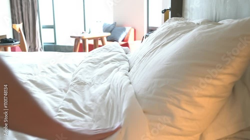 A person is pulling a white pillow off of a bed. The bed is unmade and has a white comforter