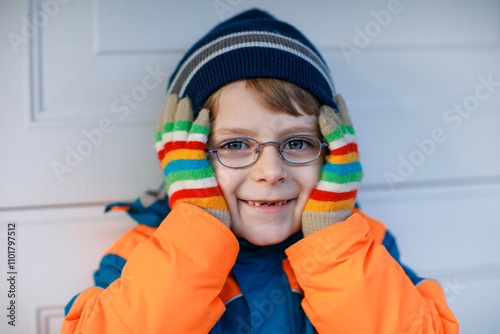 Portrait of little cute school kid boy with glasses and colorful winter fashion clothes. Child smiling and having fun with the camera. Winter, spring or autumn fashion. Kid with missing front teeth