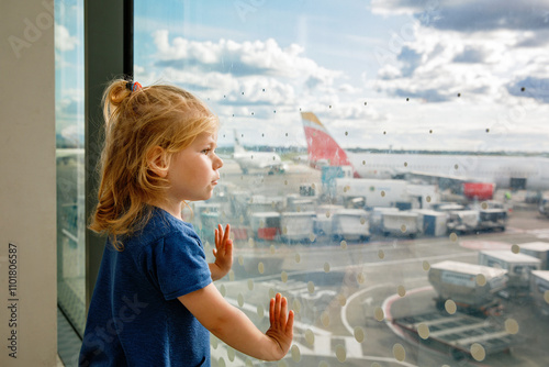 Cute little toddler girl at the airport, traveling. Happy healthy child waiting near window and watching airplanes. Family going on summer vacations by plane. photo