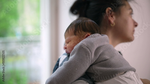 Mother cradling her newborn baby on her shoulder, gazing out of a sunlit window. serene and intimate bond between mother and child in a calm and nurturing environment