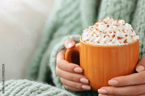 Cozy hands holding a warm cup of pumpkin spice latte topped with whipped cream