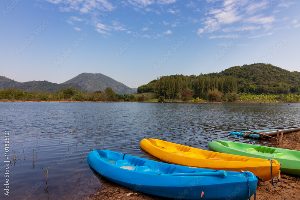 Colorful kayaks resting by a tranquil lake, surrounded by green hills and a clear blue sky, perfect for outdoor adventure and relaxation. Colorful kayaks resting by a tranquil lake, surrounded by green hills and a clear blue sky, perfect for outdoor adventure and relaxation.