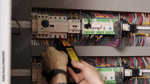 Electrician testing, Electrical connections, Electrical repairs. Close-up electrician using multimeter to test electrical connections on circuit breaker panel with colorful wiring.