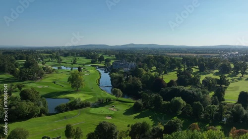 Adare, County Limerick, Ireland, September 2024. Drone rises pulling back while orbiting counter clockwise revealing manor and Franciscan Friary on the river with golf course in a stunning landscape. photo