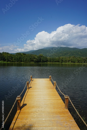 A wooden pier stretches out into a serene lake, offering a peaceful view of the surrounding mountains and clear blue sky