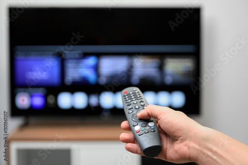 The man turned on the TV to select a program to watch and holds the remote control in his hand photo