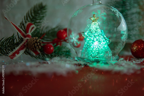 Glowing Christmas tree in a glass ornament with festive decorations in the background