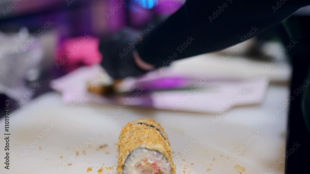 Chef handling a fried sushi roll on a white cutting board, black gloves, crispy golden crust, seafood filling, food preparation with scattered crumbs Chef handling a fried sushi roll on a white cutting board, black gloves, crispy golden crust, seafood filling, food preparation with scattered crumbs