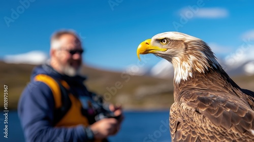 A blurred photographer with a camera is focused on a majestic eagle perched beside a tranquil lake, highlighting the intricate details of the bird's feathers. photo