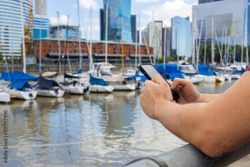 A young man holding his smartphone while visiting a popular spot in Puerto Madero, Buenos Aires, Argentina, on a sunny day