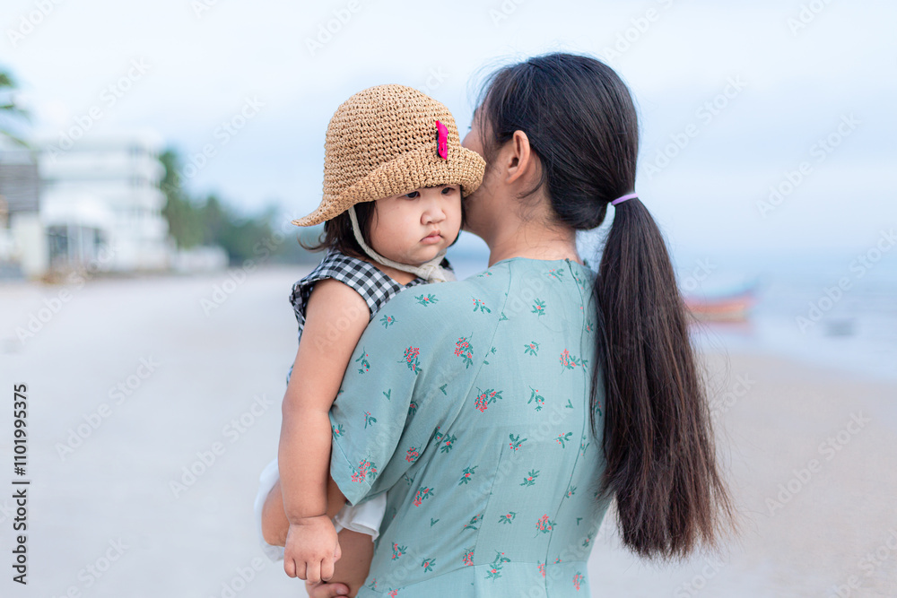 Obraz premium Mother carries her daughter on the beach,Asian mother was carrying her daughter on the beach. little girl sleeps in her mother's arms.