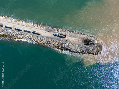 Construction activity on coastal pier with equipment and trucks during daylight