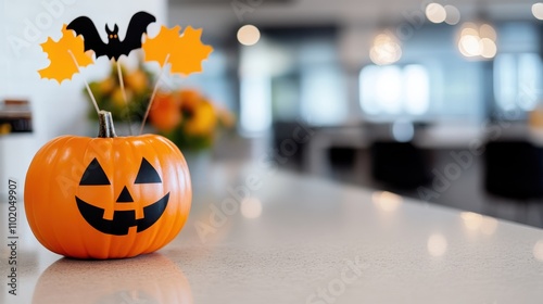 An orange pumpkin topped with bat and autumn leaf accents sits on a smooth table surface, creating a festive and whimsical focal point for Halloween decor. photo