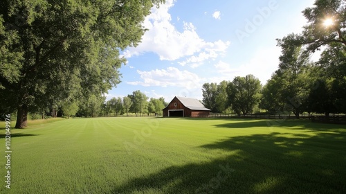 Expansive green meadow with a barn under a bright blue sky in a serene countryside setting