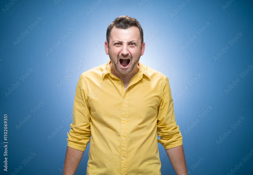 Rage man looking at camera and screaming over blue background, dresses in yellow shirt. Frustrated guy Rage man looking at camera and screaming over blue background, dresses in yellow shirt. Frustrated guy