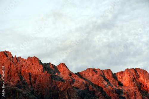 Rot leuchtende Bergkette mit wolkigem Himmel im Hintergrund (Alpenglühen)
