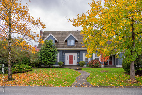 Two story stucco luxury house with garage door, big tree and nice Fall foliage landscape in Vancouver, Canada, North America. Day time on November 2024.
