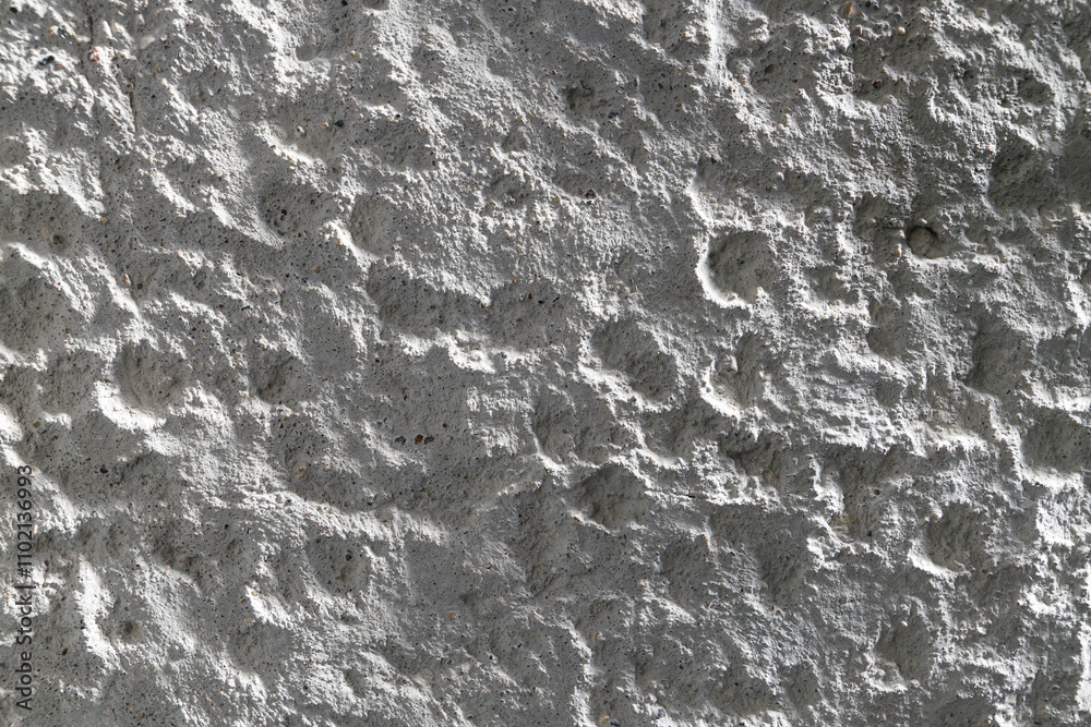 Fototapeta premium A white wall features a rich texture with intriguing patterns and shadows, illuminated by soft natural light.