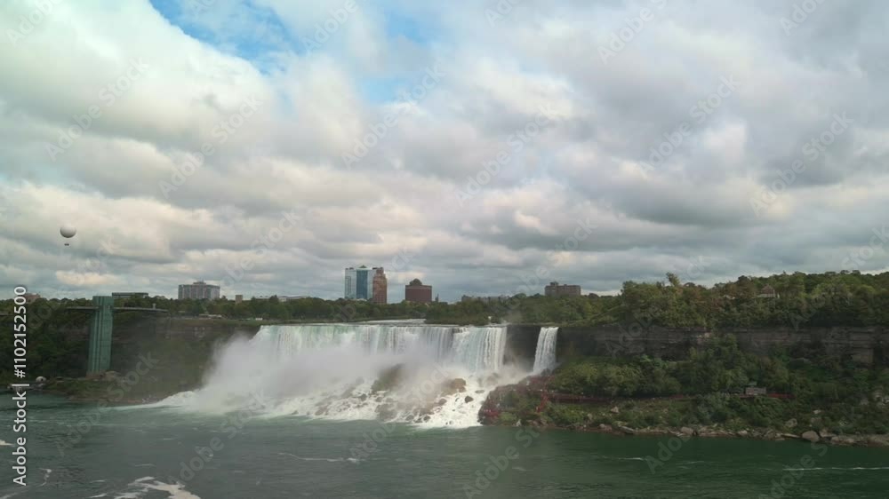 Wide view of Niagara Falls cascading amid lush greenery with city skyline in distance under partly cloudy sky blend of nature urban scenery Niagara Falls with city skyline Niagara Falls city skyline Wide view of Niagara Falls cascading amid lush greenery with city skyline in distance under partly cloudy sky blend of nature urban scenery Niagara Falls with city skyline Niagara Falls city skyline