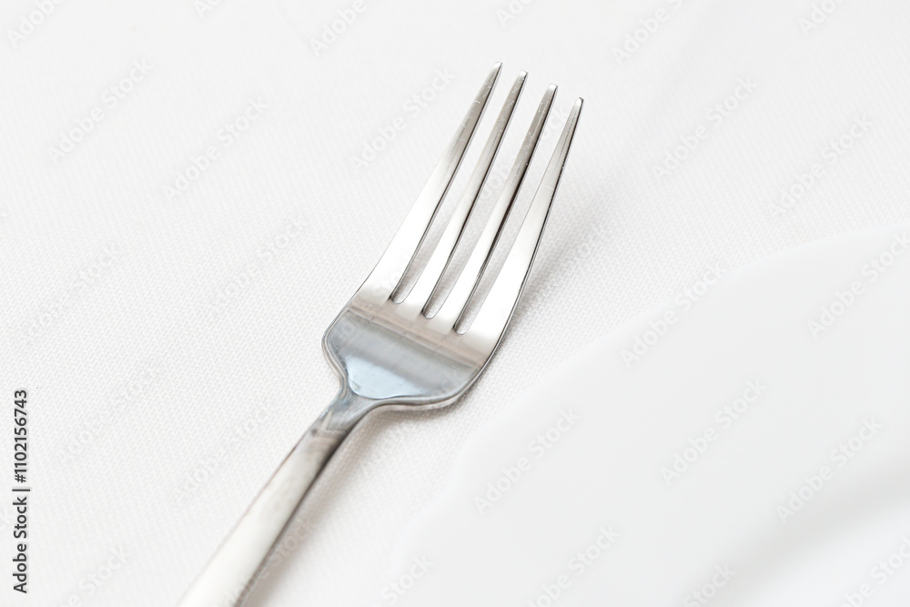 Single silver fork on a white table cloth next to a plate. Closeup of elegant dishware in a luxury dining setting. Minimalist table arrangement with clean, shiny cutlery background. Single silver fork on a white table cloth next to a plate. Closeup of elegant dishware in a luxury dining setting. Minimalist table arrangement with clean, shiny cutlery background.