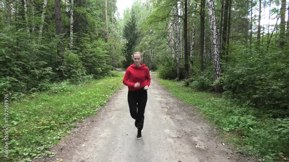 Front view of woman jogging along path in forest Front view of woman jogging along path in forest