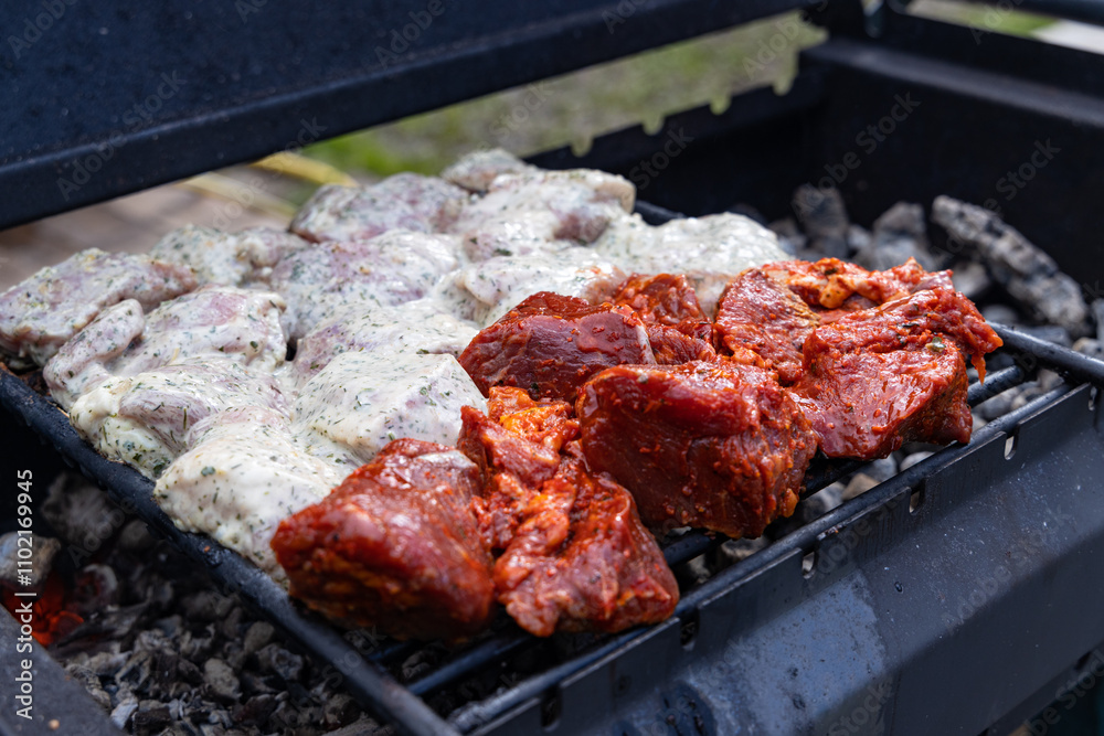 Close-up of seasoned meat grilling on a hot charcoal grill, with a mix of marinated and raw pieces. Close-up of seasoned meat grilling on a hot charcoal grill, with a mix of marinated and raw pieces.