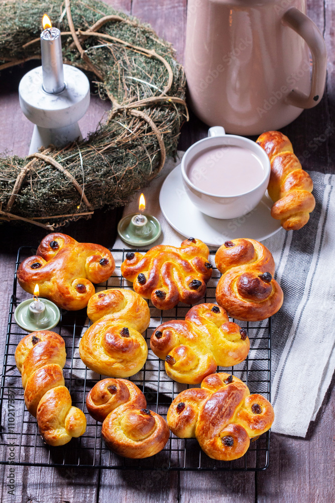 Traditional saffron Swedish buns lussekatt in different shapes, served with cocoa on a wooden table. Buns for St. Lucia's Day.