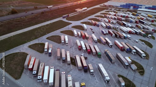 Drone shot of truck parking in Europe seen from above. Aerial footage of rows of vehicles parked for rest at a service station. Neatly placed trucks arranged at a truck stop seen from a helicopter.
