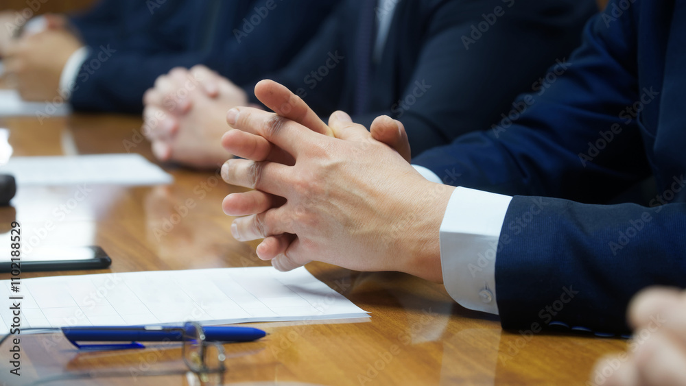 Obraz premium Folded hands of a politician or businessman sitting at a table next to colleagues. Work meeting or negotiations. Official, manager, lawyer or deputy. No face. Selective focus