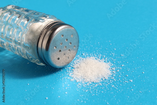  On a blue background lies an overturned salt shaker with salt. photo