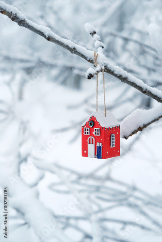 Festive winter background. red Christmas toy house hang on snowy tree branch. Christmas and new year holidays. symbol of cozy, loving family home. fairy tale atmosphere in winter season