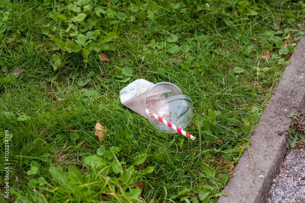 Plastikowe opakowanie po napoju z rurką wyrzucone na trawę.
