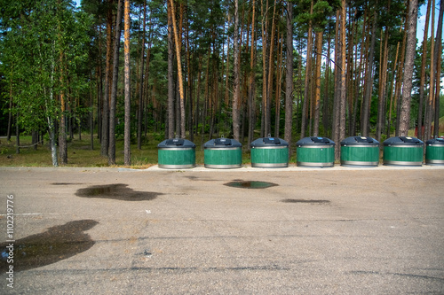 Obraz na płótnie Zielone kontenery pojemniki na śmieci ustawione wzdłuż lasu na betonowym placu.
w salonie