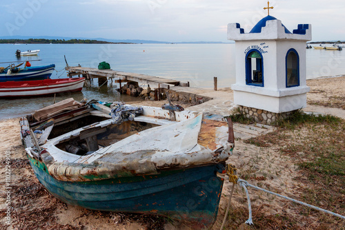 A small fishing pier with old boats and a traditional whitewashed shrine dedicated to Saint Nicholas in the evening, at Vourvourou, Sithonia, Chalkidiki peninsula, Central Macedonia, Greece photo