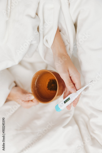 Person in bed with thermometer and cup of tea, showing signs of illness photo