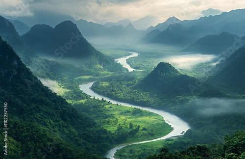 Winding river gracefully flows through dense green mountains under a misty sky at dawn