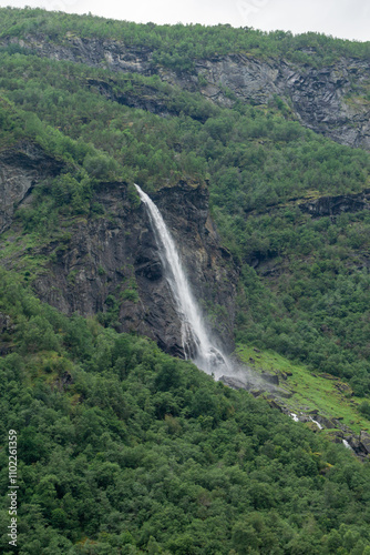 View of the Cave waterfall-Høgabru in Flåmsdalen valley, between Flam and Myrdal, Norway, surrounded by lush green vegetation, rocky cliffs, and cascading water on a cloudy day photo