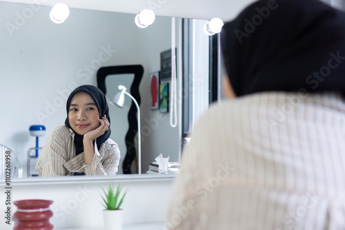 Beautiful confident asian muslim woman looking in the mirror while smiling and cheering up herself. Indonesian islam woman with hijab self motivating in front on make up mirror. photo