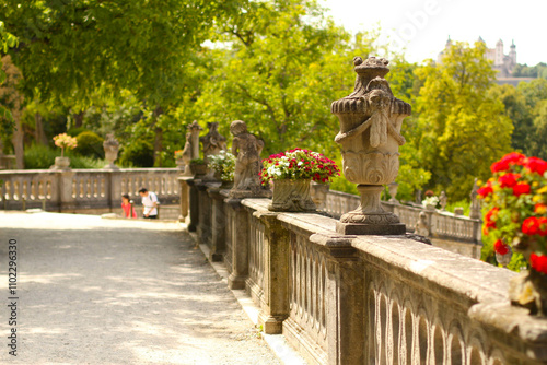 Historische Steingeländer mit dekorativen Blumenkübeln und Statuen im Sonnenschein. Eine malerische Parklandschaft, die Ruhe und Eleganz ausstrahlt. Perfekt für Reisefotografie oder Architektur