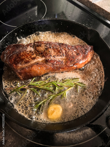 searing steak in skillet with rosemary and butter