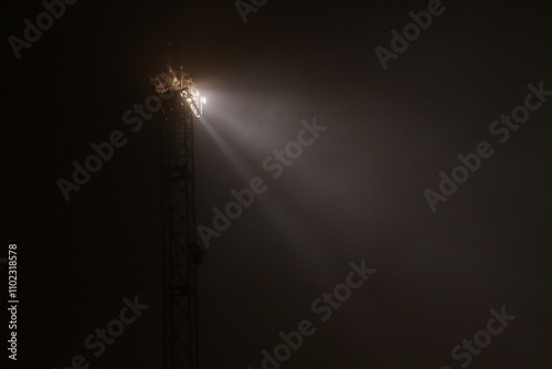 A tower with floodlights illuminates the port in the fog at night