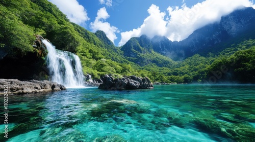 A powerful waterfall dramatically cascading down into a lush green valley, complemented by rocky terrains and enshrouded by a backdrop of towering mountain peaks.