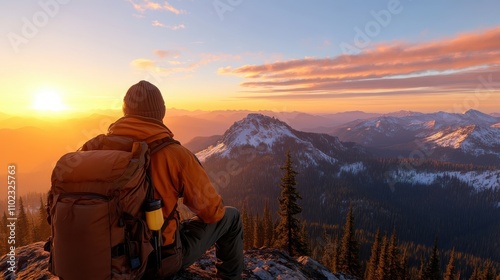 A lone backpacker, wearing an orange jacket and beanie, sits atop a mountainous peak at sunrise, taking in the stunning panoramic views of distant peaks.