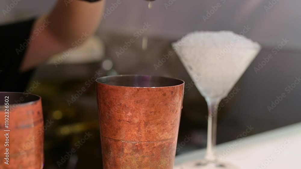 Bartender pouring juice into a copper cocktail shaker with a martini glass filled with crushed ice in the background, showcasing mixology skills and preparation Bartender pouring juice into a copper cocktail shaker with a martini glass filled with crushed ice in the background, showcasing mixology skills and preparation