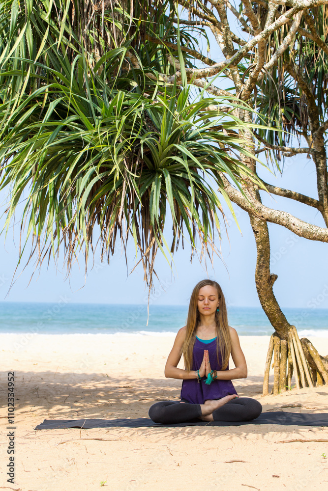 A woman is sitting on the beach, meditating under a palm tree