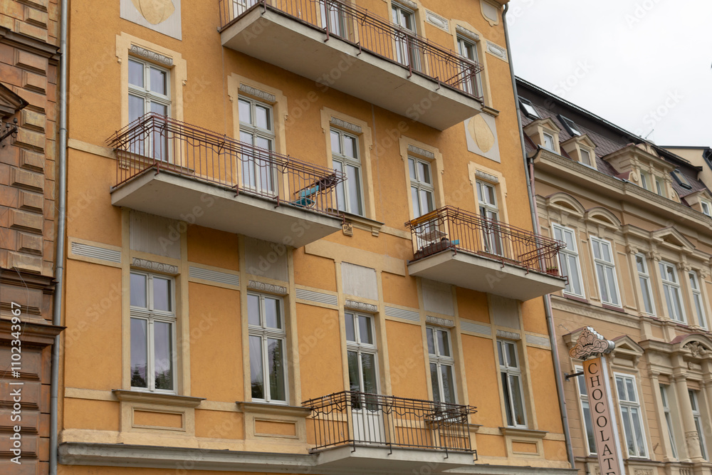 A bright yellow building featuring multiple balconies and windows, standing out distinctly against a cloudy sky on an overcast day A bright yellow building featuring multiple balconies and windows, standing out distinctly against a cloudy sky on an overcast day
