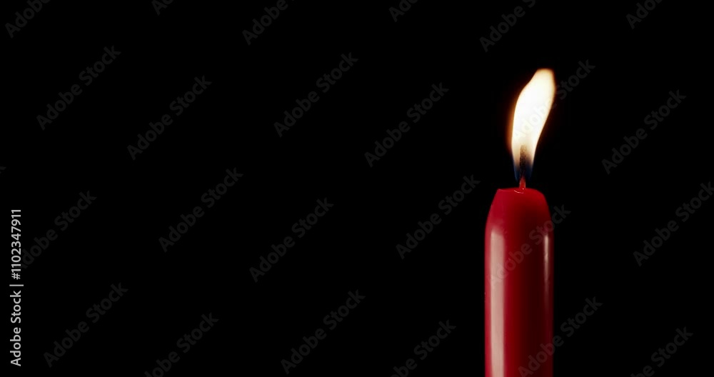 A single red candle burning. Isolated candle burning with dark background. Red paraffin candle with yellow shades burns on a black background. Background or illustration of remembrance or celebration. A single red candle burning. Isolated candle burning with dark background. Red paraffin candle with yellow shades burns on a black background. Background or illustration of remembrance or celebration.
