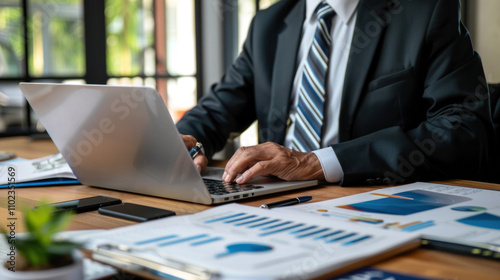 Senior man sitting at desk with laptop, handling important documents, managing finances or business matters.